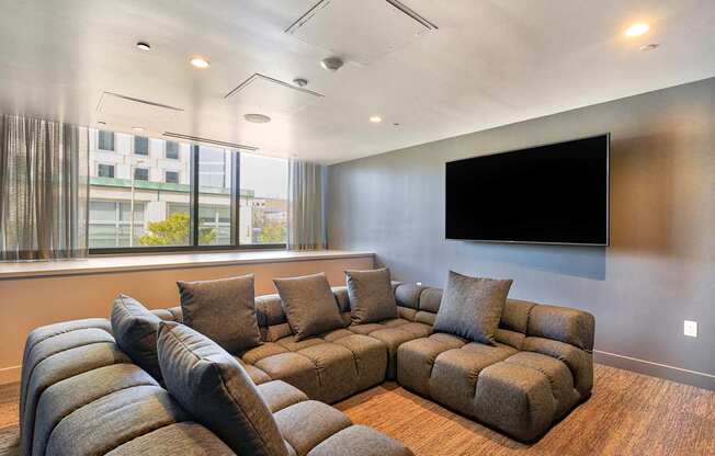A living room with a large sectional sofa and a flat screen TV mounted on the wall.