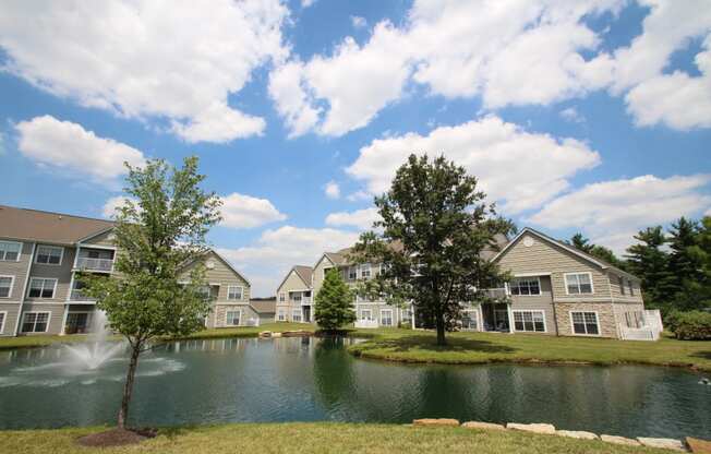This is a picture of a fountain in a pond with building exteriors at Nantucket Apartments, in Loveland, OH.