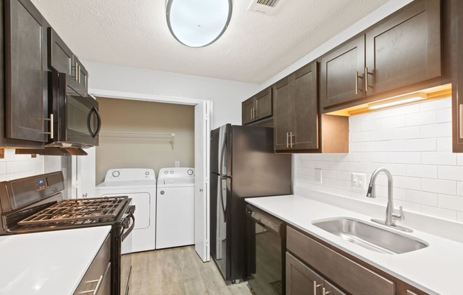 Newly renovated kitchen with black appliances, solid surface white countertops, dark wood cabinetry and complimenting wood like plank flooring.  full size washer and dryer in the closet