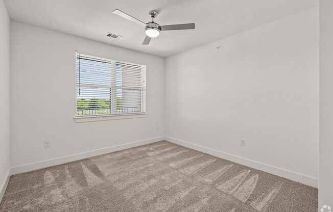 A room with a fan, carpet, and a window.