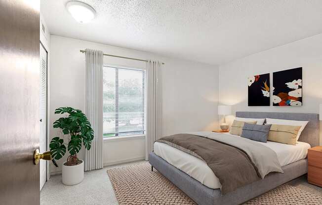 A bedroom with a bed, nightstand, window and a plant at Old Monterey Apartments in Springfield, MO