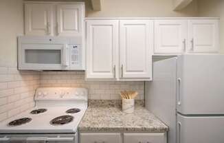 A kitchen with white cabinets and white appliances in a 1 bedroom, 1 bath apartment home at Harvard Square Apartments in the Vickery Midtown neighborhood of Dallas, TX.