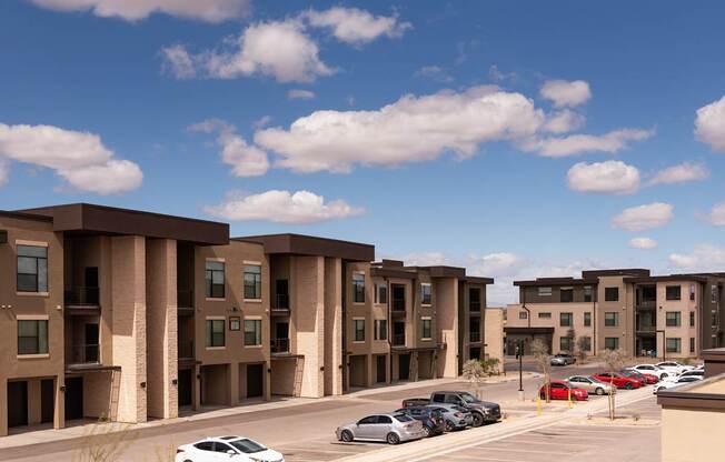 A row of apartment buildings with cars parked in front.