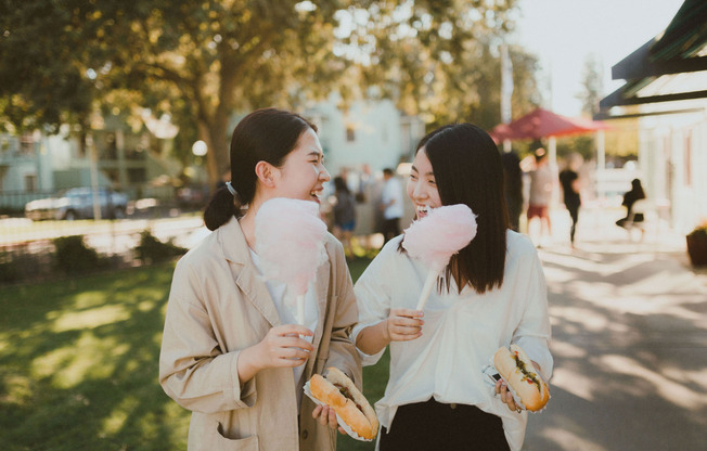 Two young women holding cotton candy and smiling at eachother