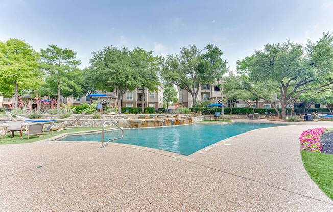 A large outdoor swimming pool surrounded by trees and a concrete patio.