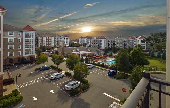 A sunset view of a parking lot with cars parked and a pool in the distance at Vermella Lyndhurst apartments, Lyndhurst, New Jersey