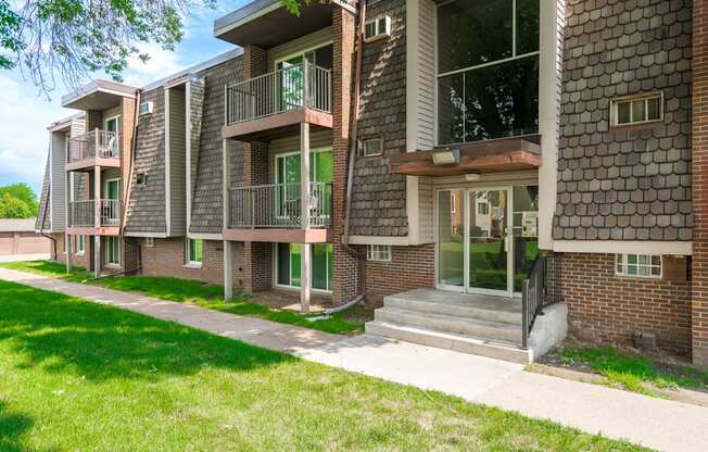 an exterior view of a brick apartment building with a sidewalk and grass