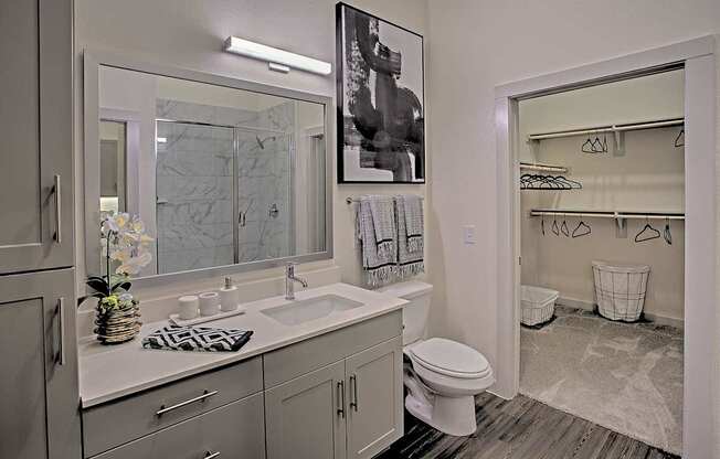 A bathroom with a sink, mirror, toilet and a shower.
