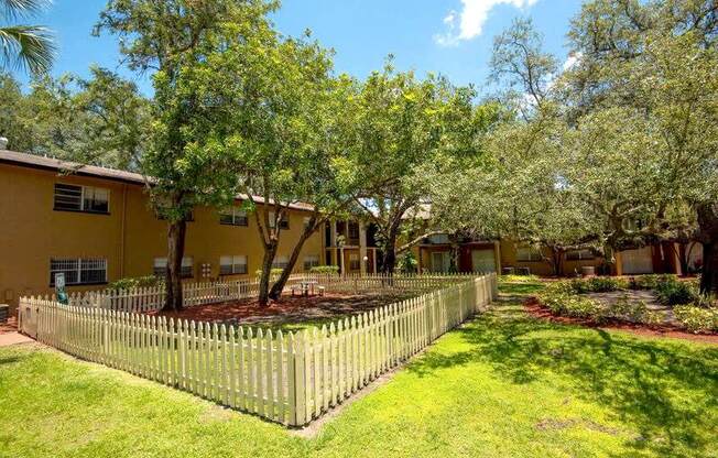 a yard with a fence and trees in front of a yellow house