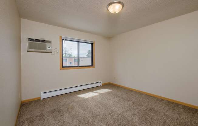 a bedroom with a window and a carpeted floor. Fargo, ND Birchwood 2 Apartments