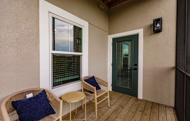 a porch with two chairs and a table and a green door