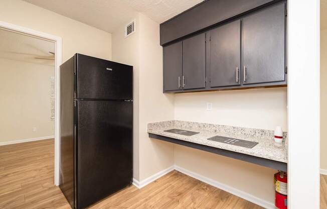 A black fridge in a kitchen with wooden floors and black cabinets.