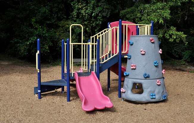 A playground with a pink slide and a grey rock climber.