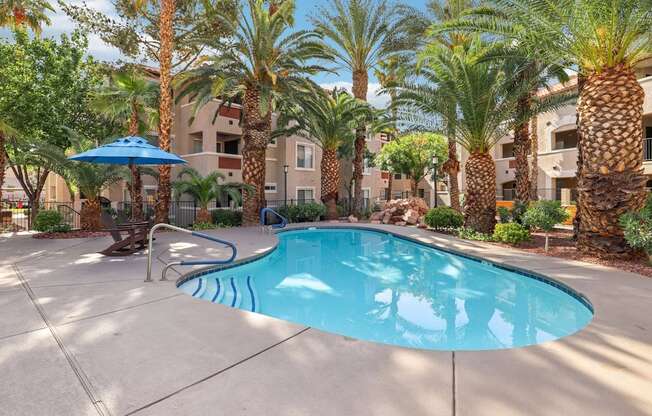 A pool surrounded by palm trees and a blue umbrella.
