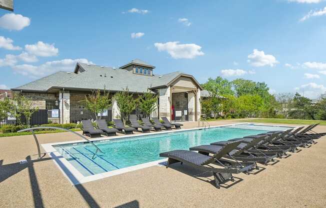 A pool with sun loungers and a building in the background.