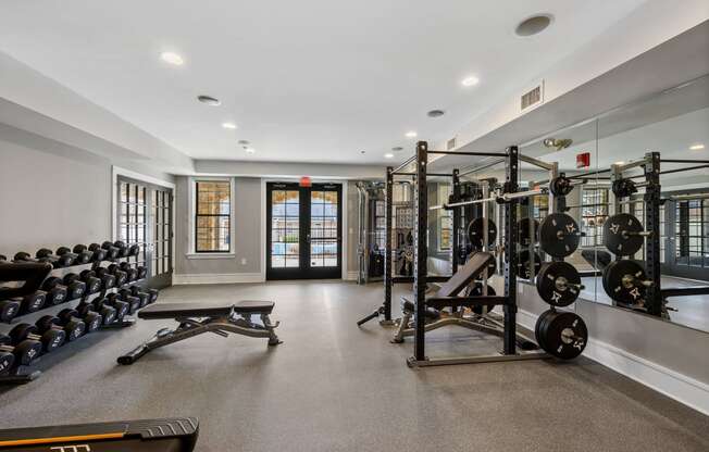 A fitness center with free weights, weight equipment, a window, large mirrors, and double doors leading to a resort-style swimming pool.