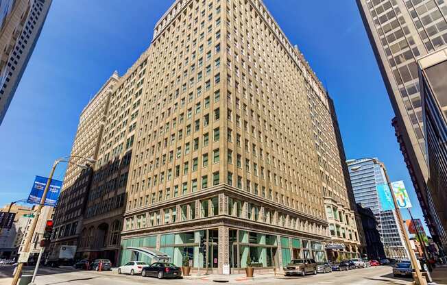 A large tan building with many windows is in the middle of a city street.