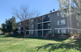 a gray apartment building with a green lawn and trees