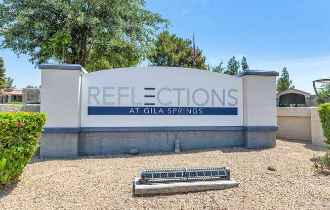 A sign that says "Reflections at Gila Springs" in front of some trees.