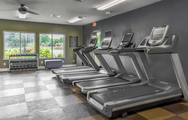 a gym with cardio equipment and chairs in a room with windows