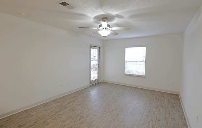 A room with a ceiling fan and two windows.