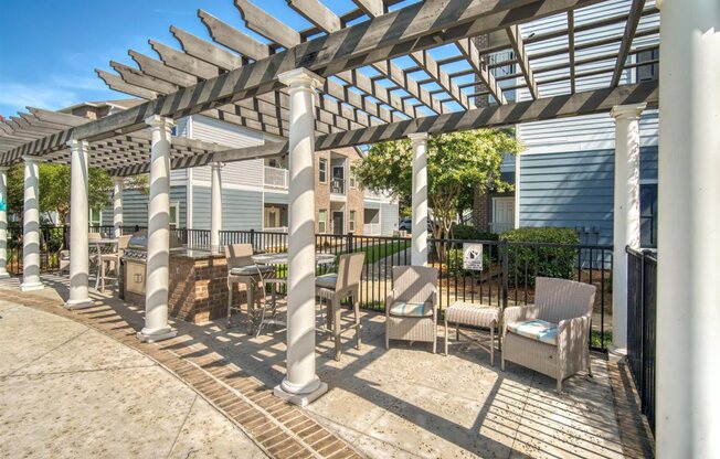 A patio with a white pergola and chairs.