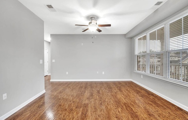 an empty living room with a large window and a ceiling fan