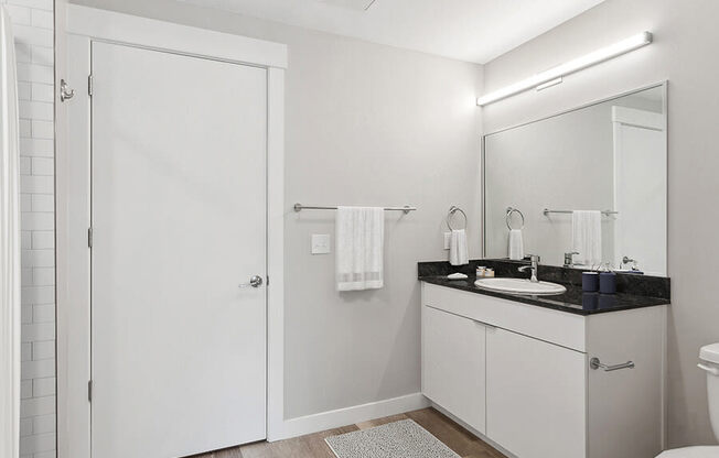 Model Bathroom with Wood-Style Flooring, White Cabinets & Shower/Tub at Seven Skies Apartments located in Sandy, UT.