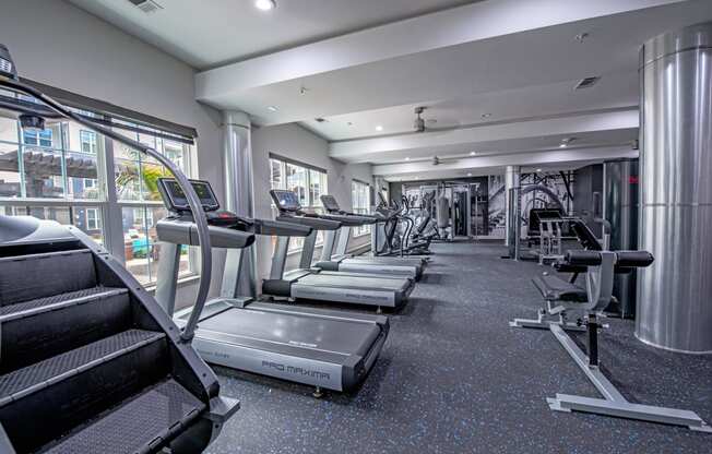 a gym with treadmills and other exercise equipment in a building with windows