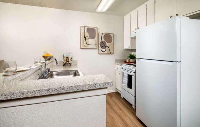 A kitchen with a white refrigerator, sink, and cabinets.