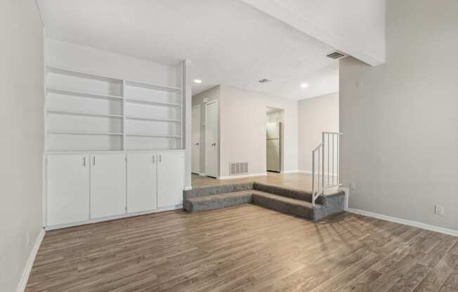 a living room with white walls and wood flooring and a staircase