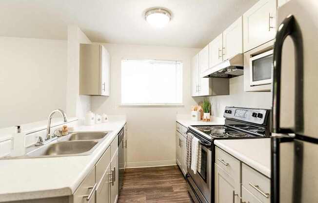 A kitchen with a black refrigerator, white cabinets, and a sink. at Crown Pointe, Lakewood, Washington