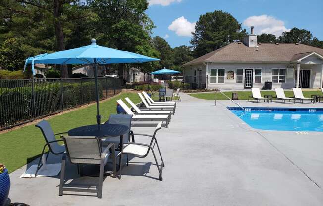 a swimming pool and patio with chairs and umbrellas