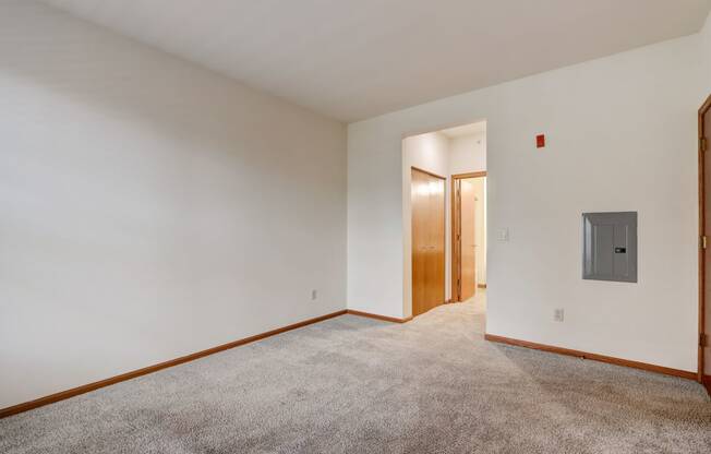 a living room with white walls and carpet and a door to a hallway