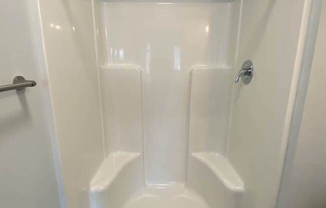 A white shower stall with a towel bar and a drain.