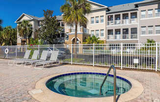 A pool with a fence and chairs in front of a building.