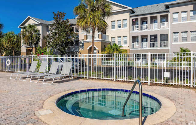 A pool with a fence and chairs in front of a building.