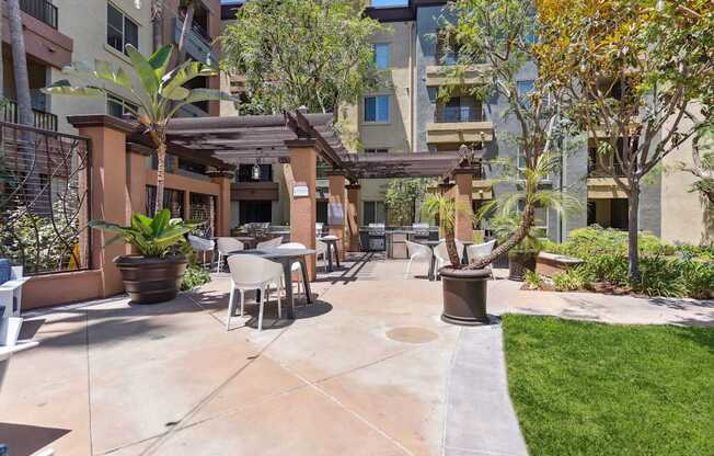 A patio area with a table and chairs surrounded by plants and trees at The Kitt at Warner Center Apartments, Woodland Hills, CA