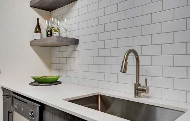 A kitchen with a white tiled wall and a stainless steel sink.