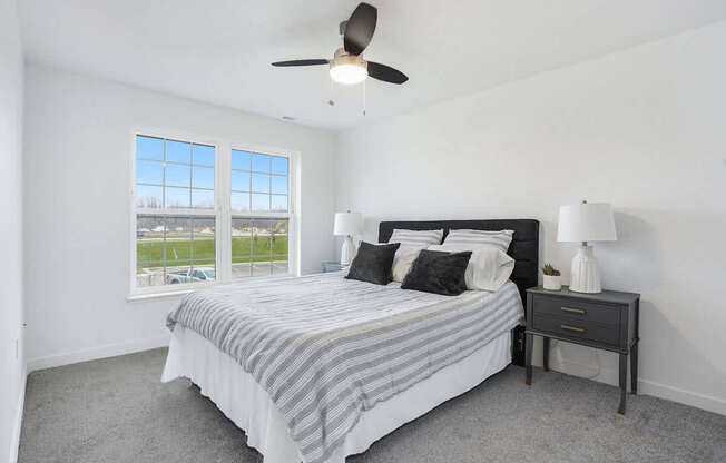 A bedroom with a bed, nightstand, ceiling fan and window at Meadowbrooke Apartment Homes in Kentwood, MI 49512