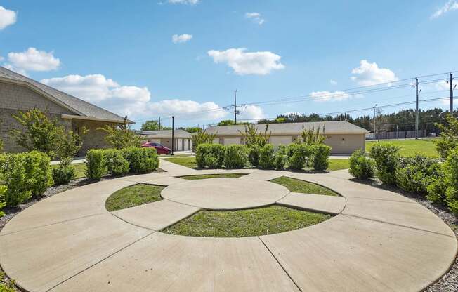 A circular garden with a central island surrounded by bushes and a building in the background.