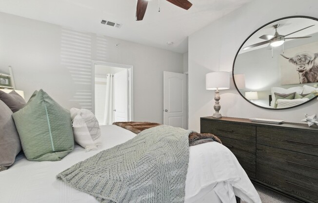 A bedroom with a bed, pillows, a blanket, a dresser, and a mirror.