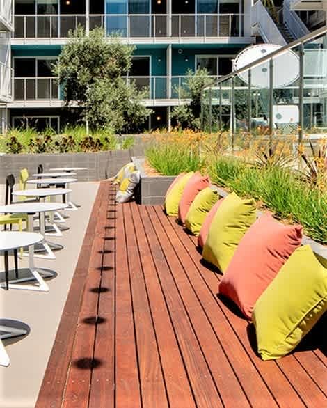 A wooden bench with orange and green cushions is in front of a building.