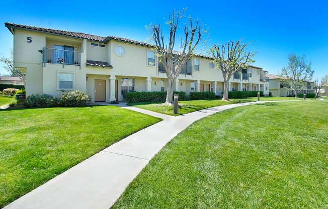 the view of an apartment building with a sidewalk and grass