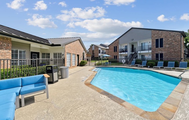 A pool with comfortable lounge chairs and a bench at The Oaks of Denton Apartments in Denton, TX