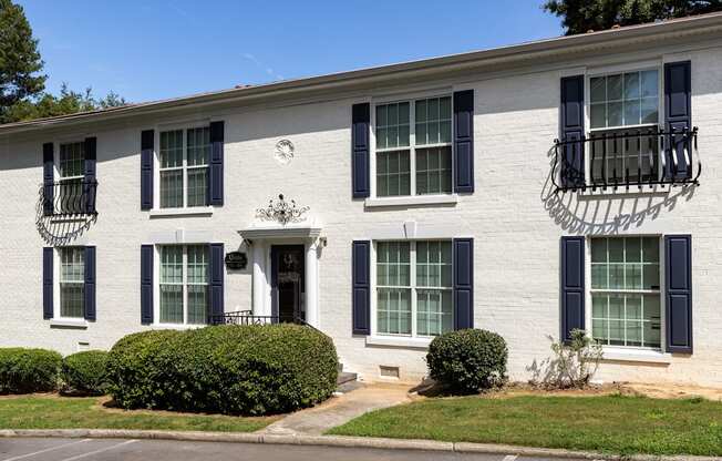 a white brick building with black window shutters and a lawn