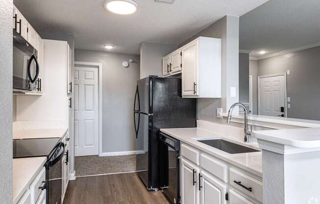A black refrigerator in a kitchen with white cabinets.