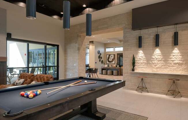 A pool table is in the middle of a room with a stone wall.