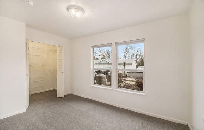 A bedroom with a grey carpet, a closet door, and a large window at West Hampton Park Apartments in Elkhorn, NE 68022