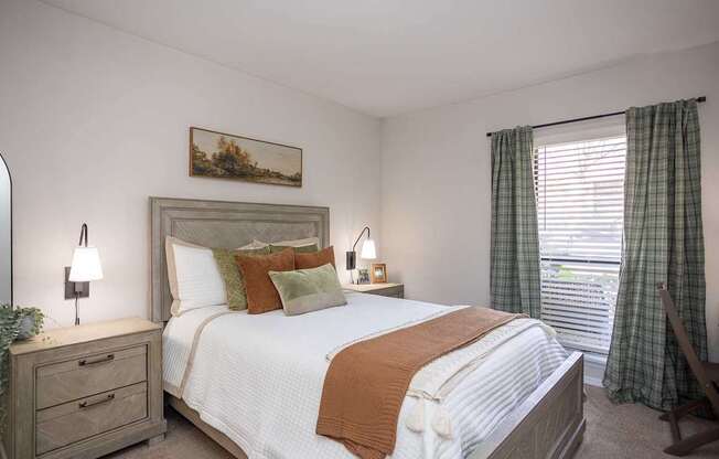 A bedroom with a large bed, a nightstand with a lamp, and a painting on the wall.